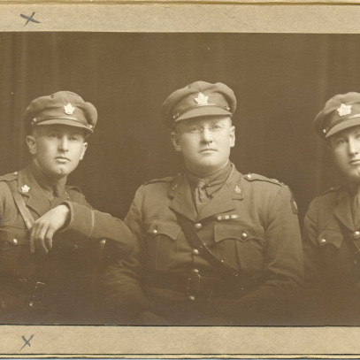 Photo en tons sépia – Trois hommes posent assis face à l’objectif de la caméra. Ils portent tous un uniforme militaire, y compris la casquette.