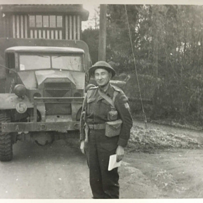 Photographie en noir et blanc – Archie reste au garde-à-vous en souriant devant un véhicule militaire.