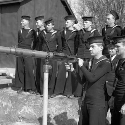 Photographie en noir et blanc – Des marins s’entraînent à manier une mitrailleuse montée sous la supervision d’un instructeur.