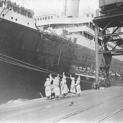 Photographie en noir et blanc – Des femmes agitent leur mouchoir sur un quai tandis que des hommes embarquent dans un navire.