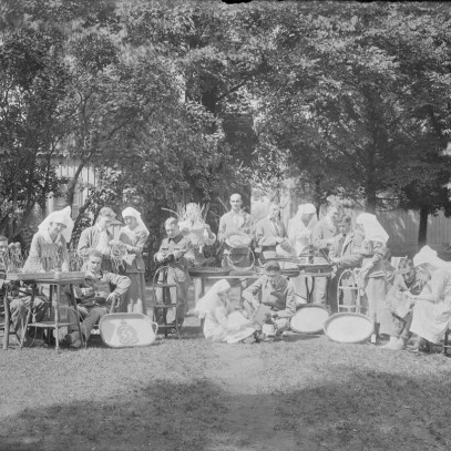 Photographie en noir et blanc – Des infirmières et des soldats sont assis sur des chaises ou sur le sol près d’un grand arbre. Ils sont en train de tisser des paniers.