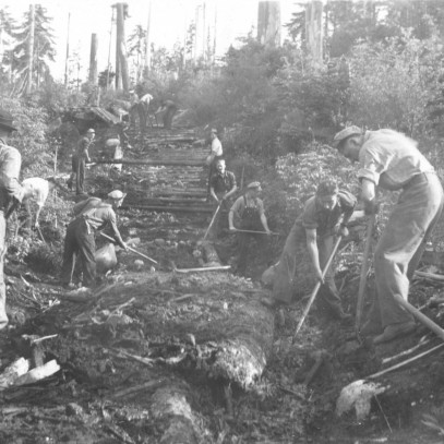Photographie en noir et blanc – Des hommes sont photographiés en train de défricher un sentier à travers une forêt pour construire une route.