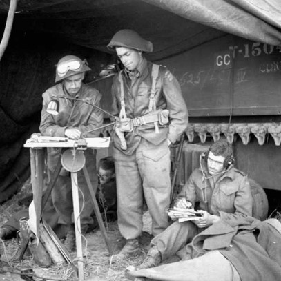 Photographie en noir et blanc – Des soldats se trouvent dans un abri de fortune construit près d’un char d’assaut.