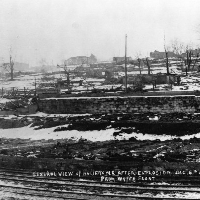 Photographie en noir et blanc – Une = ville détruite, vue du front de mer. Des structures squelettiques, des décombres et des arbres calcinés sont tout ce qui reste.