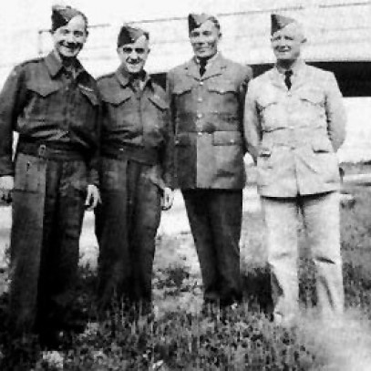 Photographie en noir et blanc – Quatre hommes en uniforme, en ligne, sourient à la caméra.