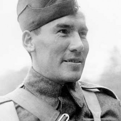 Photographie en noir et blanc – Harvey Dreaver regardant au loin, photographié à partir de la poitrine. Il porte l’uniforme complet, y compris la casquette. Une sangle traverse sa poitrine.