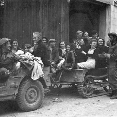 Photographie en noir et blanc – Une jeep militaire et une remorque sont remplies de civils français. Un soldat canadien conduit et quelques autres se trouvent autour.