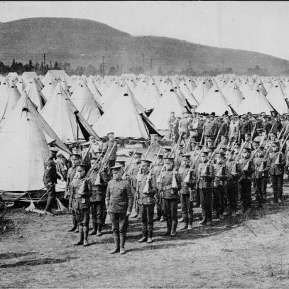 Photographie en noir et blanc Des soldats restent au garde-à-vous dans une colonne ordonnée en face d’un champ de tentes blanches en forme de cônes.