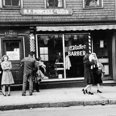 Photographie en noir et blanc – Des hommes et des femmes marchent près de vitrines saccagées, les bras pleins de marchandises.