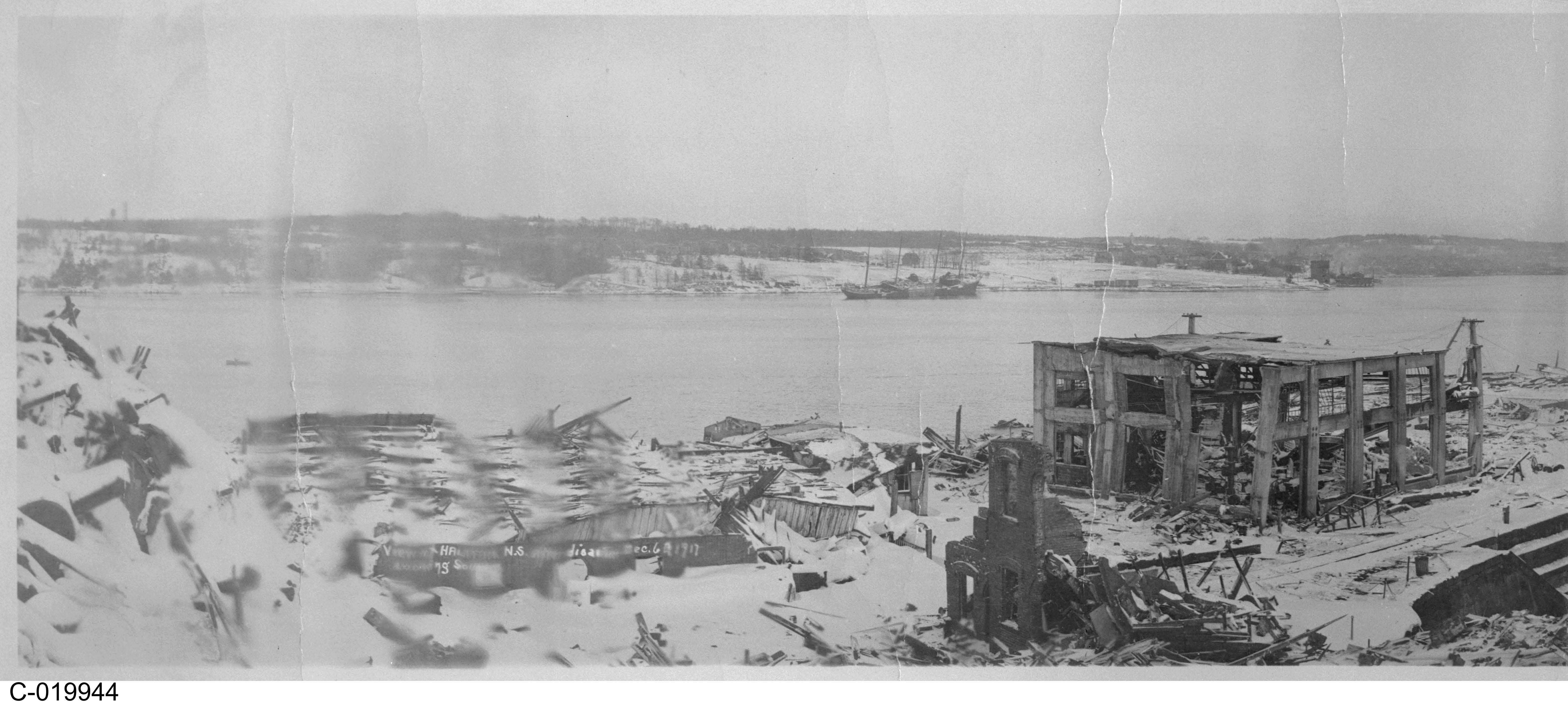 Photographie en noir et blanc – – Divers bâtiments sont montrés en ruines. Des usines fonctionnent toujours au loin. Un plan d’eau est visible à gauche sur la photo.
