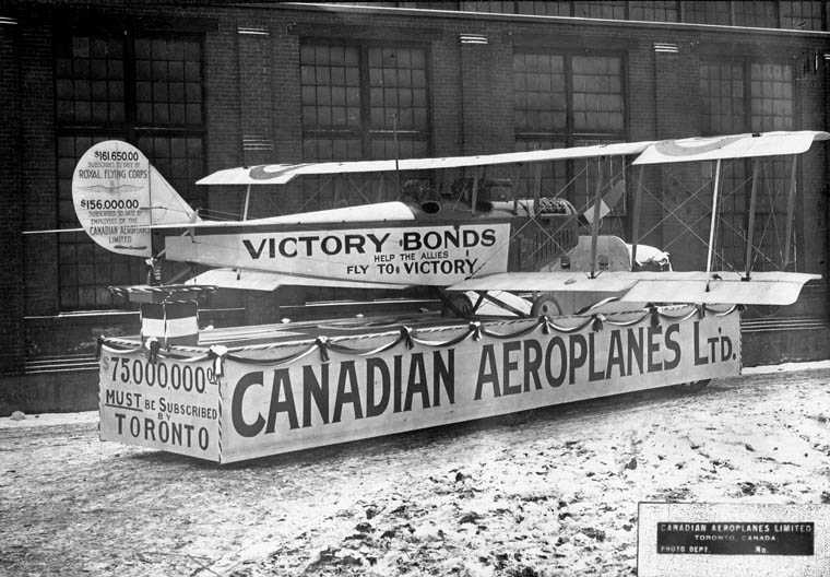 Un char transporte un avion canadien dans un défilé de l’emprunt de la Victoire. Divers slogans et messages ont été imprimés sur sa surface.