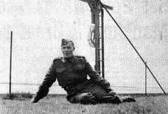 Photographie en noir et blanc – Joseph Dreaver, en uniforme, est assis, appuyé sur son bras droit et les jambes repliées sous lui. Il semble détendu.