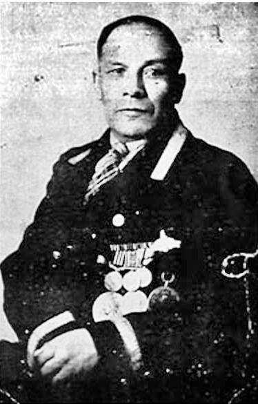 Photographie en noir et blanc – Un portrait de Joseph Dreaver le montre avec les mains repliées sur sa ceinture. Il porte un uniforme et des médailles du côté gauche.