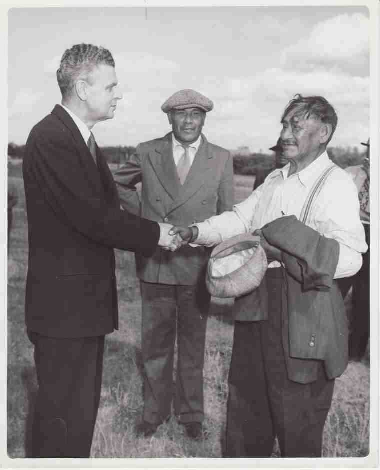 Photographie en noir et blanc – John Diefenbaker (à gauche) serre la main d’un ouvrier. Joseph Dreaver est derrière eux, au centre.