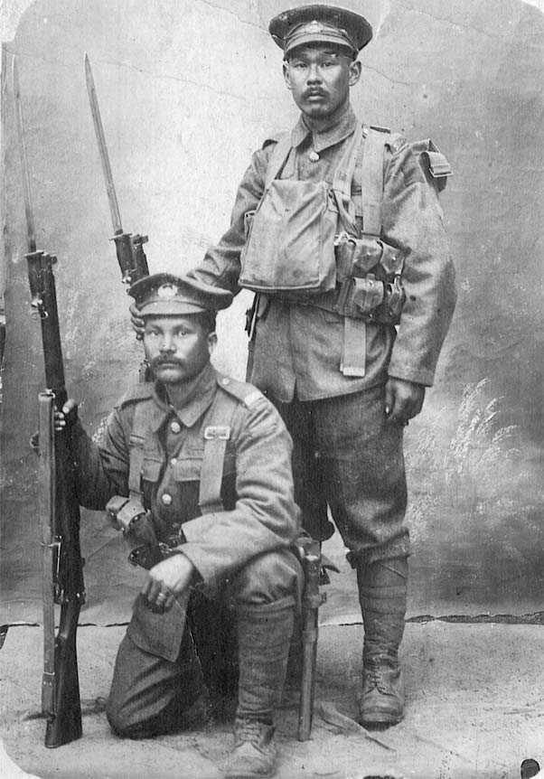 Photographie en noir et blanc – Deux hommes portant l’uniforme complet ainsi que les accessoires du Corps expéditionnaire canadien. L’un (Mitsui) est debout, alors que l’autre (Shishido) est à genou. Les deux tiennent des fusils auxquels sont fixées des b