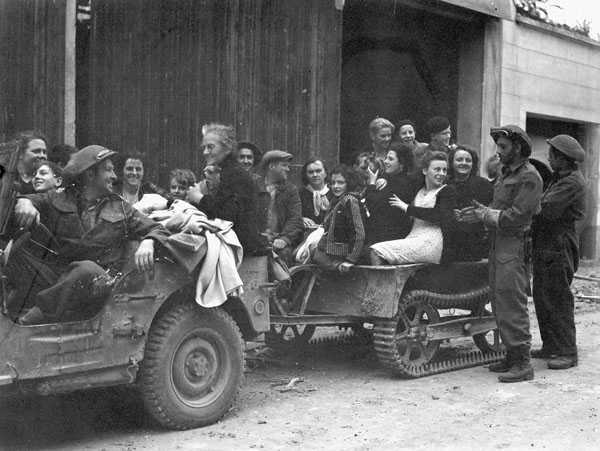 Photographie en noir et blanc – Une jeep militaire et une remorque sont remplies de civils français. Un soldat canadien conduit et quelques autres se trouvent autour.