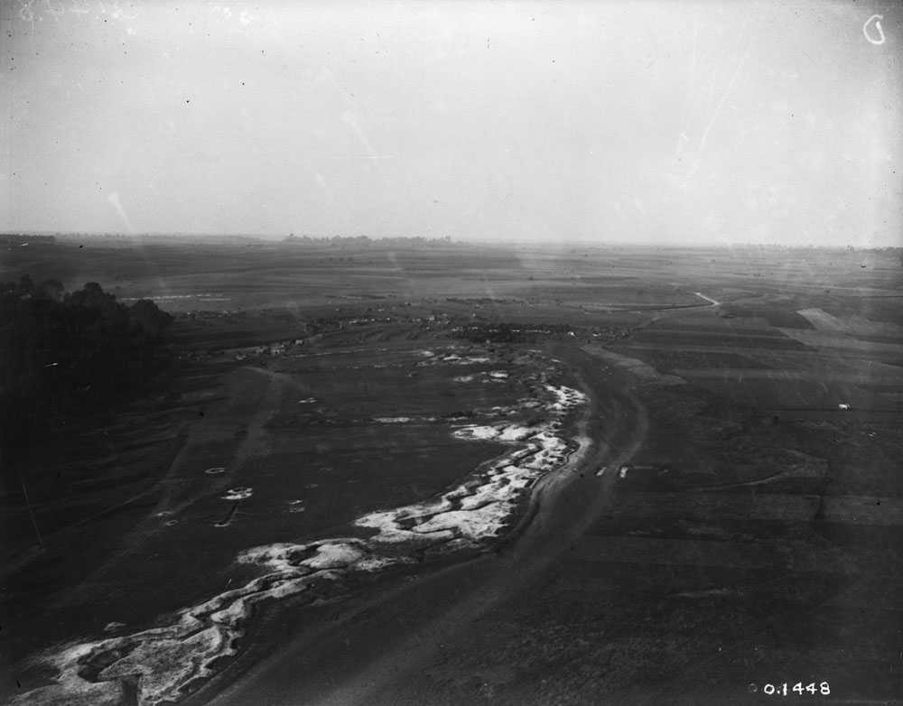 Photographie en noir et blanc – Vue aérienne de lignes de tranchées sur le champ de bataille de la Somme. Un labyrinthe de tranchées étroites coupe en diagonale le centre de l’image. On aperçoit autour de lui une étendue de champs grêlés de cratères.